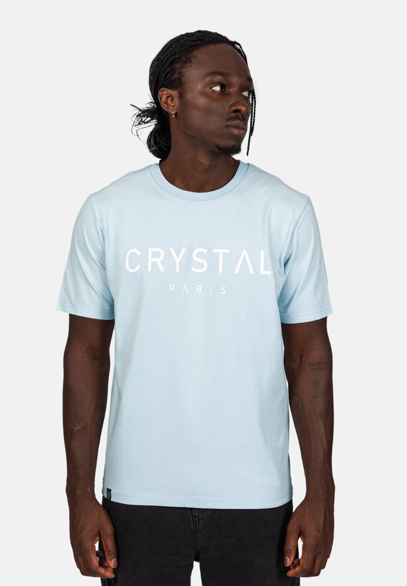 Světle modré bavlněné tričko s krátkými rukávy, kulatým výstřihem a výrazným bílým textem "CRYSTAL PARIS" přes hruď.