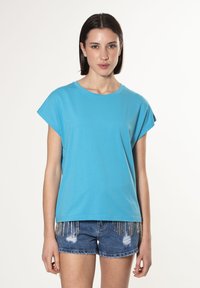 Turkis oversized t-shirt lavet af bomuld, med korte ærmer og rund halsudskæring, parret med slidte denim shorts med metal accenter.