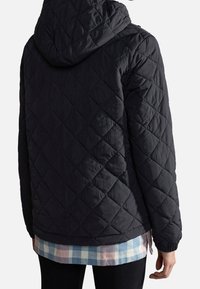 Person i en sort vatteret jakke med hætte, lagd ovenpå en blå og pink ternet skjorte, vist fra ryggen.