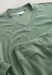 Grønt fleece sæt i to dele til afslapning med V-hals top og bukser med elastisk talje. Har blød tekstur og ribbede manchetter. Simpelt design.