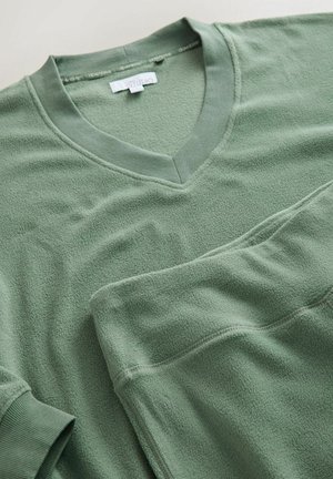 Žalios vilnos dviejų dalių poilsio drabužių komplektas su V formos iškirpte ir elastinga juosmens juosta. Pasižymi minkšta tekstūra ir raukšlėtomis rankogaliais. Paprastas dizainas.