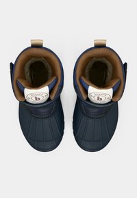 Bottes imperméables bleu marine avec une semelle en caoutchouc texturé, doublure rembourrée marron et une sangle Velcro. Présente un logo circulaire sur le côté.