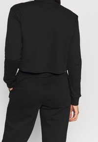 Sudadera corta negra con mangas largas, hecha de una tela suave. Destacan los puños acanalados y el dobladillo recto.