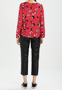 Blusa rossa a fiori con accenti neri e bianchi, maniche a sbuffo e scollatura rotonda, abbinata a pantaloni in pelle nera a Capri e sneaker nere.