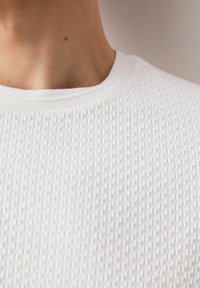 White textured top with a grid pattern, featuring a round neckline and ribbed trim, highlighting a lightweight fabric.