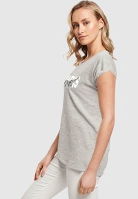 Graues T-Shirt mit kurzen Ärmeln, runder Ausschnitt und einem bedruckten Grafik auf der Vorderseite, getragen mit weißen Slim-Fit-Hosen.