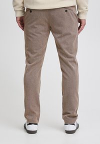 Béžové kalhoty s texturou a rovný střihem, s dvěma zadními kapsami se černými knoflíky a kapsou na pravé straně na zip.