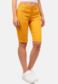 Geel denim Bermuda shorts met een aansluitend ontwerp, voorzien van voorzakken en contrasterende stiksels. Gecombineerd met witte sneakers.