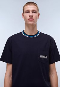 Námořnická modrá bavlněná tričko s kulatým výstřihem, s vícebarevným pruhovaným límečkem a náprsní kapsou s výšivkou značky.