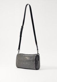 Black textured bag with a cylindrical shape, covered in small silver studs, and featuring an adjustable black strap for shoulder carry.