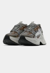 Παχιά αθλητικά παπούτσια με γκρι επάνω μέρος από δίχτυ και συνθετικό υλικό, με καφέ λεπτομέρειες σε σχέδιο λεοπάρδαλης, παχιά λευκή μεσαία σόλα και μαύρη λαστιχένια εξωτερική σόλα.