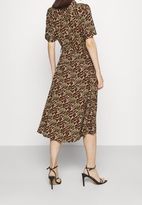 Un lungo vestito a maniche corte caratterizzato da un motivo a stampa animale in marrone e verde. Ha una vita stropicciata e scende fino a metà polpaccio. Indossato con tacchi neri.