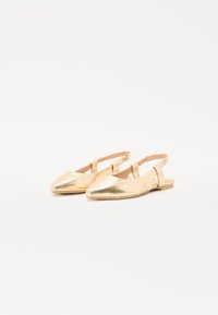 Ballerines slingback métalliques dorées avec un bout pointu, une texture lisse et une simple sangle au niveau de la cheville. Semelle plate avec des détails de design minimalistes.