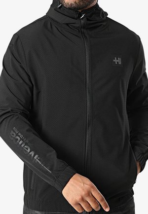 Veste noire avec une finition texturée, fermeture éclair à l'avant et capuche réglable. Logo sur la poitrine et design textuel le long de la manche. Matériau léger.