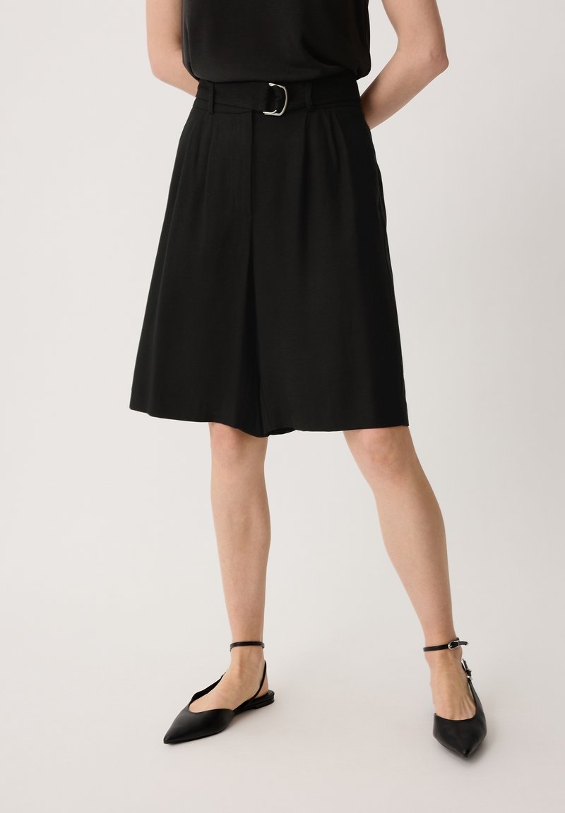 Shorts noirs taille haute avec une jambe large, détail de ceinture avec une boucle en argent, et une texture de tissu lisse et léger.