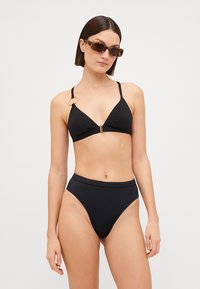 Svart bikini-sett med en teksturert, triangel-formet topp med justerbare stropper og et gull-accent, kombinert med høy-skåret matchende truser.