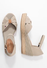 Wedge espadrillas beige con dettaglio a fiocco in tessuto, suola in juta intrecciata e cinturino alla caviglia regolabile. Texture liscia con leggeri accenti.