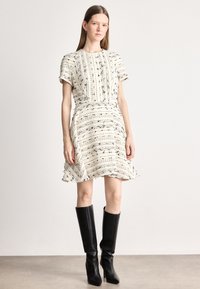 Balta kleita ar melnām strukturētām līnijām un īsām piedurknēm, izplūdušs svārku dizains, komplektā ar melnām augstiem zābakiem līdz ceļgaliem. Tīrs, mūsdienīgs dizains.