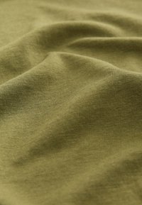 Měkká olivově zelená látka s viditelnou jemnou pletenou texturou a jemnými záhyby vytvářejícími decentní stíny a zvýraznění.