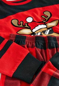 Red and black pajama set featuring a reindeer graphic with sunglasses. Long sleeves and elastic waistband with ribbed cuffs. Soft fabric texture.