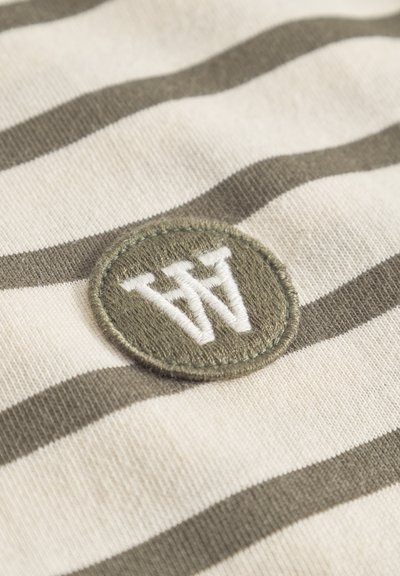Striped cotton fabric in cream and olive green featuring an embroidered circular patch with "W" logo in white.