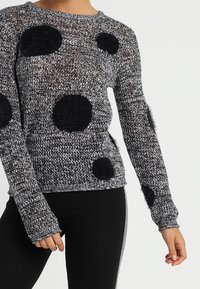 Pull en maille noire et grise avec des pois noirs duveteux, manches longues et encolure ronde ; la texture semble douce et chaude.