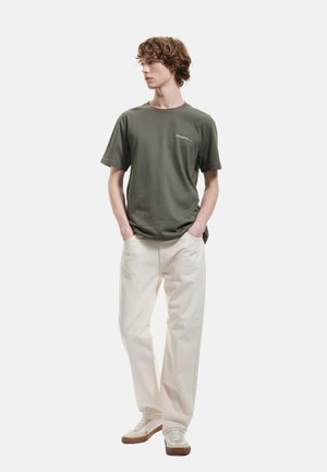 Camiseta de algodón verde oliva de mangas cortas y cuello redondo. Combinada con pantalones sueltos en color blanco roto y zapatillas crema con suelas marrones.