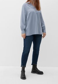 Helles blaues Bluse mit langen Ärmeln, V-Ausschnitt und gerafften Manschetten, kombiniert mit dunkelblauen Jeans und schwarzen Stiefeletten mit dicker Sohle.