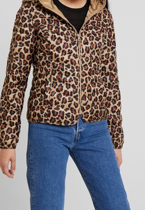 Kurtka puchowa w panterkę, zapinana na zamek, noszona z niebieskimi dżinsami i czarnym topem pod spodem, pokazana od ramion do bioder.