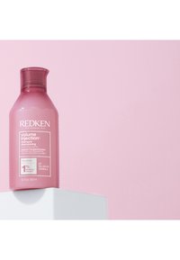Shampoo Redken Volume Injection dans une bouteille transparente rose, avec un couvercle à charnière, une étiquette blanche et un texte indiquant équilibré en pH et complexe à 1%.