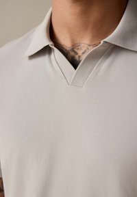 Lys grå polo t-shirt med V-halsdesign, fremstillet af et blødt struktureret stof og med korte ærmer. Kravekanter er pænt afsluttet.