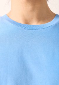 Svetlo modra bombažna majica s kratkimi rokavi, okroglim izrezom z rebrastim robom, gladkim teksturo in brez vidnih vzorcev ali poudarkov.