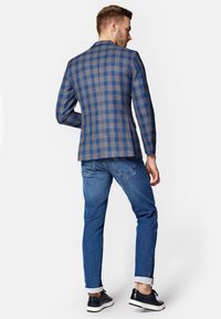 Sukienka w kratę w odcieniach niebieskiego z brązowymi akcentami, w połączeniu z podwiniętymi dżinsami. Czarne buty z białymi podeszwami dopełniają outfit.