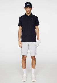 Marineblå pikétröja, ljusgrå shorts, vita sneakers och en handske. Pikétröjan har en logotyp; ensemblet är avslappnat och välsittande, lämpligt för sport.