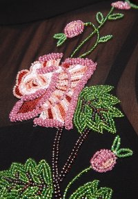 Svart tyg med intrikat pärlbroderi i blommönster i rosa, vitt och grönt, med detaljerade blad och knoppar tillverkade av olika pärlstorlekar.