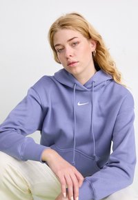 Casaco capuz roxo feito de tecido suave, com um bolso frontal, cordões de ajuste e um pequeno logotipo da Nike em branco no peito.