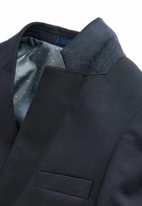 Close-up af en mørkeblå blazer med en notched krave, tekstureret stof, brystlomme og lyseblåt for med polkaprikker.
