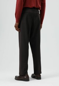 Donkere broek met krijtstreep en een getailleerde pasvorm, voorzien van een tailleband en een gladde textuur, gecombineerd met bruine leren schoenen.