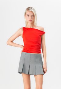 Top rojo de un solo hombro con detalles fruncidos, combinado con una mini falda gris con plisados. El top es ajustado, hecho de una suave tela texturizada.