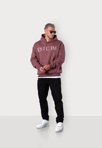 Maroon hoodie with white "ESTEEM" text, kangaroo pocket, ribbed cuffs, worn with black distressed jeans and white sneakers.