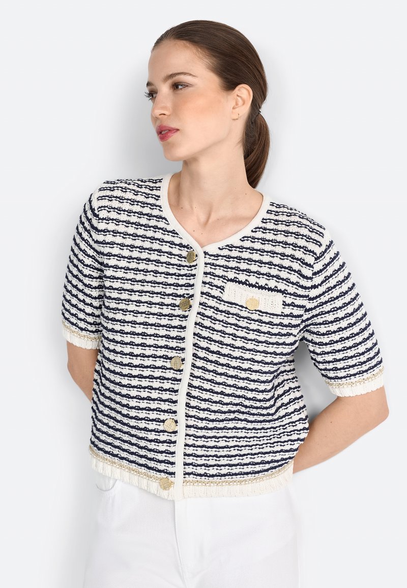 Cardigan rayé bleu marine et blanc avec des manches courtes, tissu texturé, encolure ronde et boutons dorés, comportant une petite poche avant.