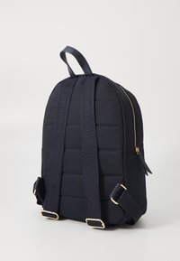 Mochila de tela de navegación acolchada con textura suave, cremallera dorada y correas grabadas. Correas ajustables y asa superior para un transporte versátil.