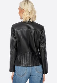 Giubbotto di pelle nera con cuciture strutturate, retro aderente e texture a coste in vita. Maniche lunghe e design del colletto classico.