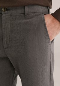 Szürke, könnyű anyagból készült, texturált nadrág oldalzsebekkel és gombos derékpánttal. Tiszta vonalak és finom minta jellemzi.