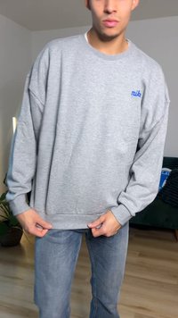 Sweatshirt cinzenta com punhos e bainha canelados, apresentando um logótipo azul "Nike" no peito. Usada com jeans azul-claro, mostrando um ajuste descontraído.