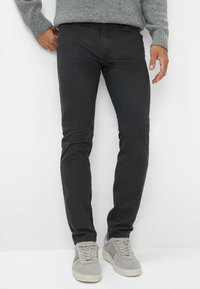 Zwarte slim-fit chinos met een zachte textuur, subtiele stikseldetails en een middenhoge taille. Gemaakt in combinatie met lichtgrijze sneakers.
