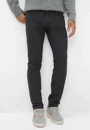 Zwarte slim-fit chinos met een zachte textuur, subtiele stikseldetails en een middenhoge taille. Gemaakt in combinatie met lichtgrijze sneakers.