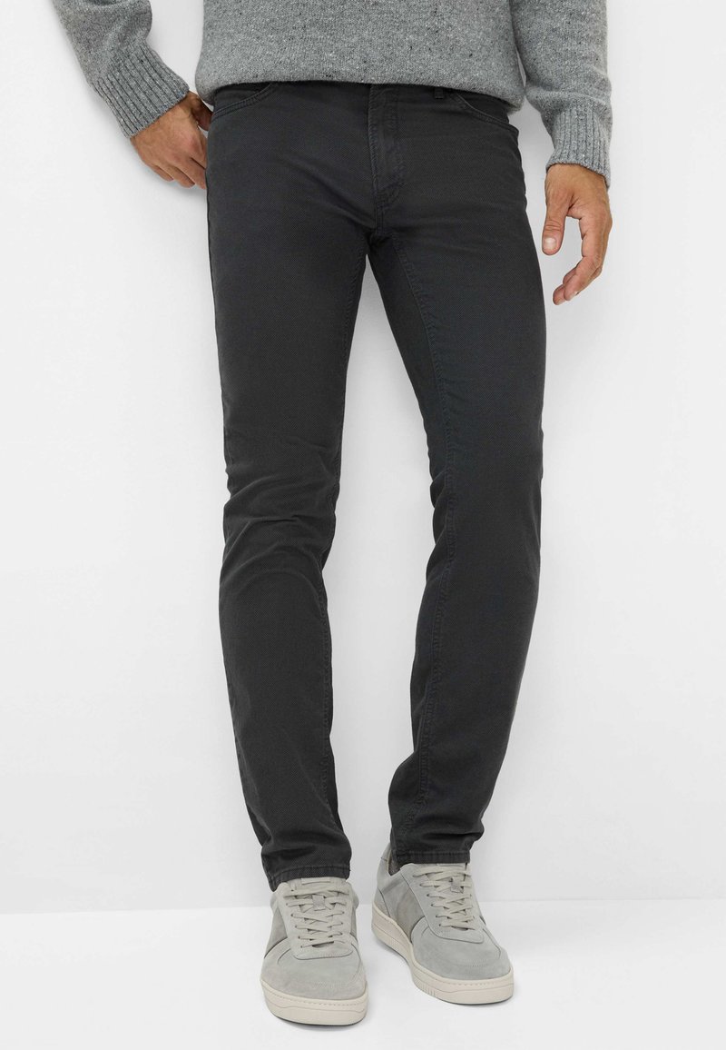 Zwarte slim-fit chinos met een zachte textuur, subtiele stikseldetails en een middenhoge taille. Gemaakt in combinatie met lichtgrijze sneakers.
