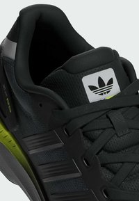 Sort og grå sportsko med en tekstureret overdel, polstret krave og neongrønne detaljer på sålen; inkluderer et logo-tag.