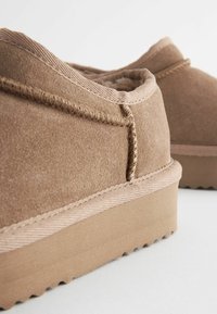 Chaussures en daim marron avec un dessus texturé, dotées d'un fin liseré en tissu clair et d'une épaisse semelle en caoutchouc plate avec un motif en zigzag.
